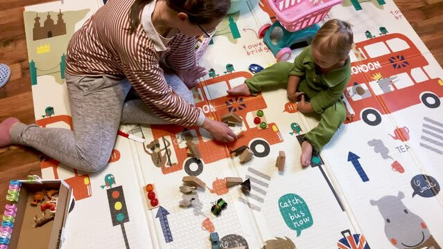 Toddler is playing with mommy in the family farm. The boy and the mother are sitting on the carpet with the domestic animals playset