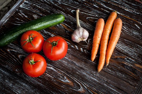Appetizing composition of fresh vegetables on a wooden dark textured table. Carrots, garlic, tomatoes and ripe cucumber. Image for your creative design or decoration.