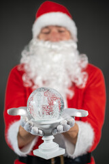 
Portrait von einem verkleideten Weihnachtsmann mit einer Schneekugel in der Hand vor grauen...