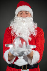 
Portrait von einem verkleideten Weihnachtsmann mit einer Schneekugel in der Hand vor grauen Hintergrund 