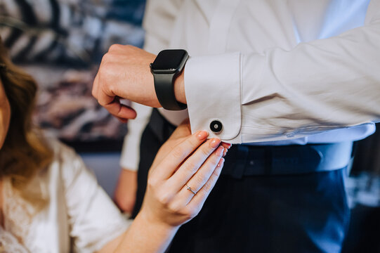 A woman, the bride cares, helps with her hand to fasten the cufflink on the groom's shirt, men with smart watches, wristwatches. Wedding photography, portrait.