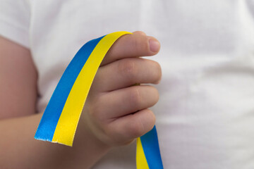 A girl in a white T-shirt holds a yellow-blue ribbon in her hand (the State Flag of Ukraine). Close-up