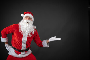 Fototapeta na wymiar Portrait von einem verkleideten Weihnachtsmann der auf einen Platzhalter zeigt und isoliert vor grauen Hintergrund ist 