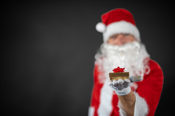 
Portrait von einem verkleideten Weihnachtsmann mit einem Geschenk in der Hand vor grauen Hintergrund 