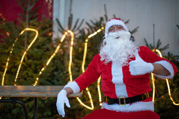 Portrait von einem verkleideten Weihnachtsmann, der auf einem Weihnachtsmarkt von Lichtern umgeben ist