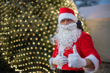 Portrait von einem verkleideten Weihnachtsmann, der auf einem Weihnachtsmarkt von Lichtern umgeben ist