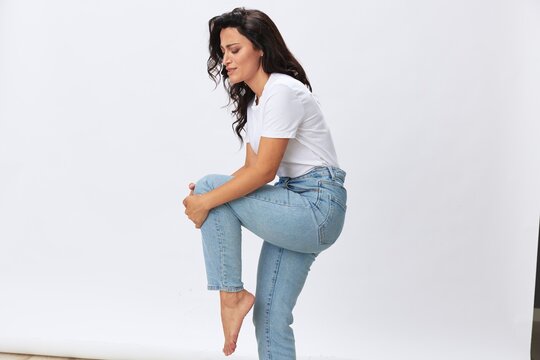 Woman leg and knee pain, leg injury, sprained joints and ligaments, wearing jeans and a white t-shirt on a white background, copy space