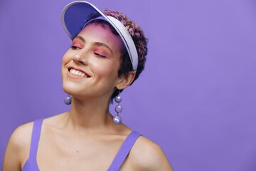 Portrait of a sporty fashion woman posing smiling in a purple sports suit for yoga and a transparent cap on a purple background monochrome