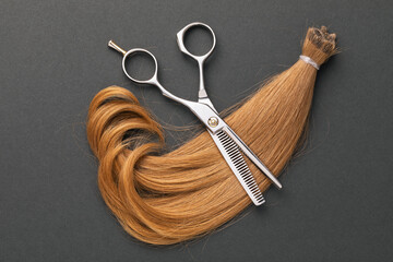 Scissors and a cut off strand of children's blond hair on a paper dark background, top view