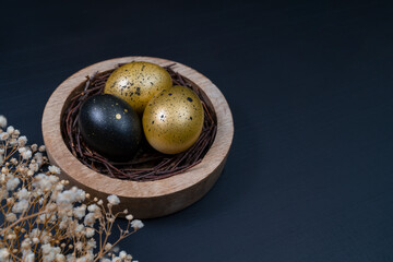 Eggs painted gold and black. Nest containing three egg with beautiful gypsophila flowers. Minimal Easter concept with copy space for text.