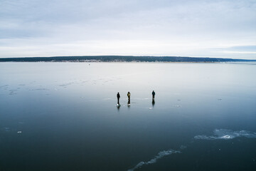 Ice fishing. Fishermen choose fishing holes on thin transparent ice without snow cover of a deep reservoir. Shooting from a drone.