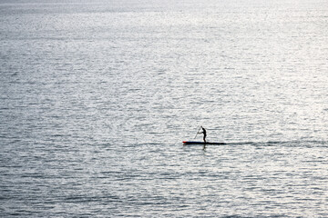 Silhouette of a woman surfing on SUP board. Active lifestyle on the ocean.