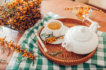 Tea with sea buckthorn berries served in cup and kettle on tray. Healthy hot drink for cold fall and winter days
