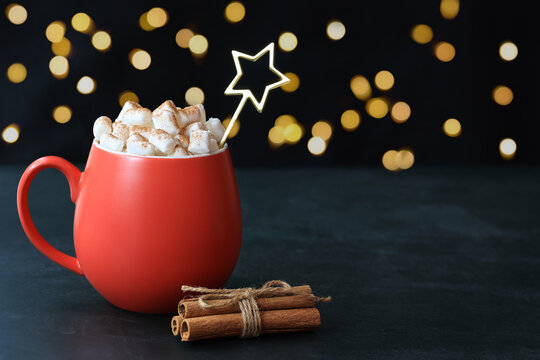Red cup, white marshmellow,star teaspoon,cinnamon sticks tied with rope, defocused lights, dark background, place for text