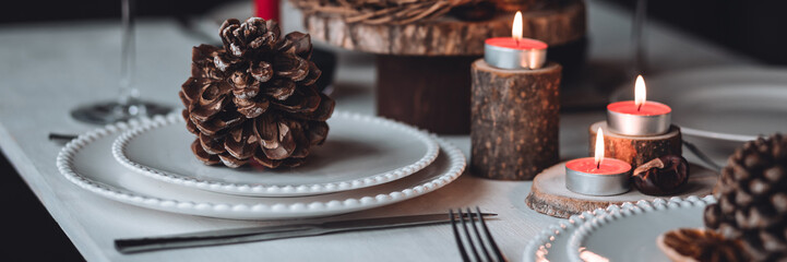 Rustic table decor for Christmas or New Year family dinner. Centrepiece with red candle, dry orange, cone, cinnamon, anise. Zero waste eco-friendly home. Cozy atmosphere, dark background. Banner