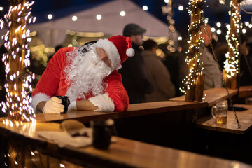 
Portrait von einem betrunkenen Weihnachtsmann, der auf einem Weihnachtsmarkt von Lichtern umgeben...
