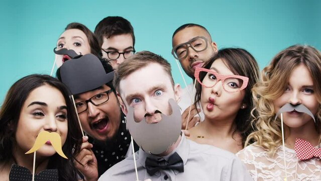 Party props, dance and group of friends in studio on blue background. Comic, goofy and people with face masks, facial disguise and dancing with silly faces while celebrating holiday or social event.