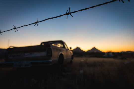 An abandoned truck rests in a field while Mount Tetakawi looms in the distance at sunrise - San Carlos, Mexico