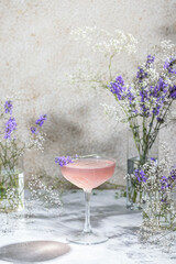 Elegant glass of Lavender Cocktail or mocktails surrounded by ingredients and fresh lavender and gypsophila flowers on gray table surface