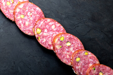 Row of salami sausage slices on a black board. Dark background