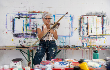 older gray haired mature happy artist woman with glasses and big paintbrushes gives thumbs up gesture