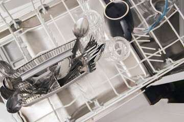 Open dishwasher with white clean dishes after washing in kitchen.