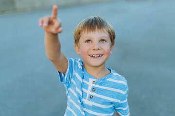 portrait of little cheerful caucasian boy pointing upwards to the sky