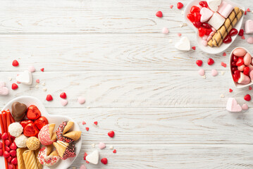 Valentine's Day concept. Top view photo of heart shaped dishes with jelly candies and pastry on white wooden desk background with copyspace