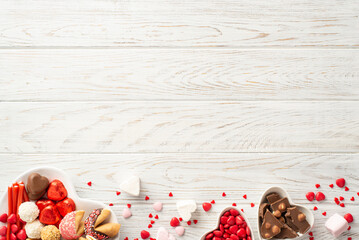 Valentine's Day celebration concept. Top view photo of heart shaped dishes with confectionery chocolate jelly candies and cookies on white wooden table background with copyspace