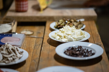 Ingredients for a home made pizza, such as greenery, ham, cheese, mushrooms, prepared on plates.