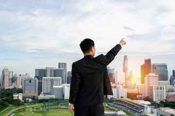 Fototapeta na wymiar businessman standing on tall building behind cityscape is pointing at goal achievement target with business success concept