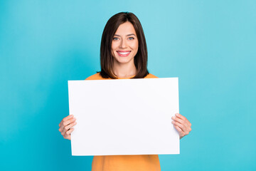 Naklejka premium Portrait of good mood adorable pretty woman with long hairstyle wear yellow t-shirt hold white poster isolated on blue color background