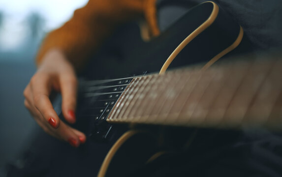 Girl playing semi-acoustic guitar at home.