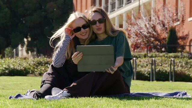 Cheerful female friends watching photos on a tablet. Best girlfriends having good time on a sunny morning in the park. High quality 4k footage