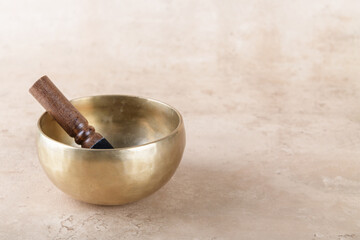 Tibetan singing bowl with stick used during mantra meditations on beige stone background, copy space. Sound healing music instruments for meditation, relaxation, yoga, massage, mental health