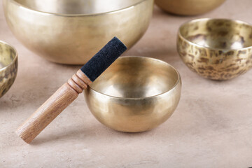 Tibetan singing bowls with sticks used during mantra meditations on beige stone background, close up. Sound healing music instruments for meditation, relaxation, yoga, massage, mental health