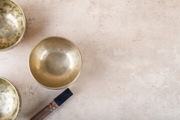Tibetan singing bowls with stick used during mantra meditations on beige stone background, top view, flat lay. Sound healing music instruments for meditation, relaxation, yoga, massage, mental health