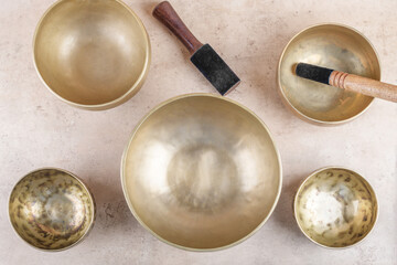 Tibetan singing bowls with stick used during mantra meditations on beige stone background, top view, flat lay. Sound healing music instruments for meditation, relaxation, yoga, massage, mental health