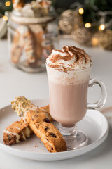A cup of white hot cocoa topped with whipped cream and served with biscotti.
