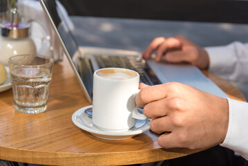 person sitting outdoors working on their laptop, cup of coffee on the table