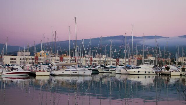 Calm crimson sunset in Porto di Lavagna in Liguria, Italy. There are a lot of siling yachts are parking in boat marina.