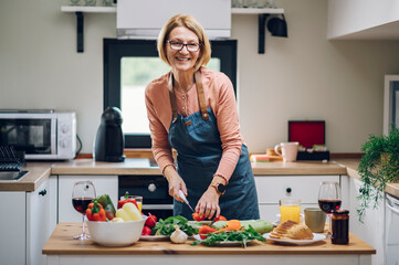 Senior woman in apron preparing food at the kitchen counter and cooking a meal