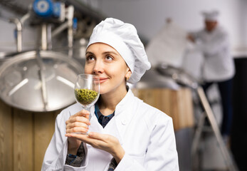 Portrait of a positive female brewer with a glass of hops at the brewery