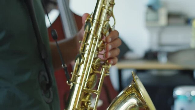 Close up tilt down shot of professional musician playing saxophone during rehearsal with band in studio