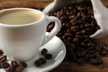 Cup of hot aromatic coffee and roasted beans on wooden table, closeup. Space for text