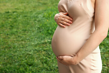 Fototapeta na wymiar Pregnant woman touching belly on green grass, closeup. Space for text