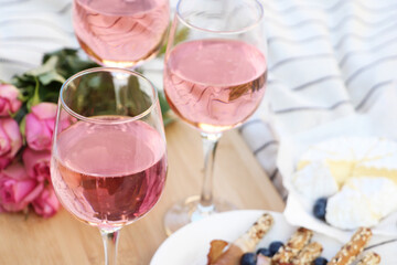 Glasses of delicious rose wine, flowers and food on white picnic blanket, closeup