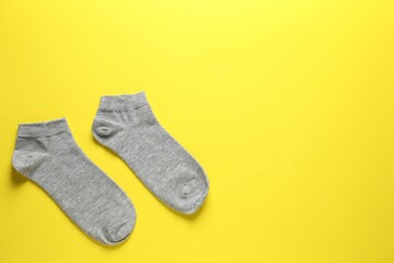 Pair of grey socks on yellow background, flat lay. Space for text
