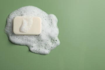 Soap and fluffy foam on green background, top view. Space for text
