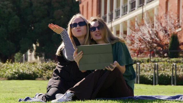 Best girlfriends having good time on a sunny morning in the park. Young, caucasian women using a tablet on active, adventurous leisure outdoors. High quality 4k footage